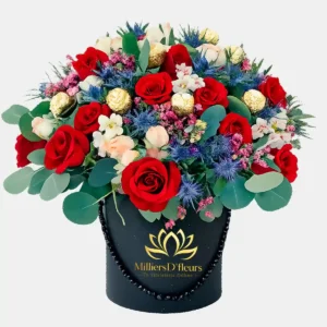 "Caja cilíndrica negra con rosas rojas, chocolates Ferrero Rocher, flores azules de cardo y eucalipto de Milliers D'fleurs."